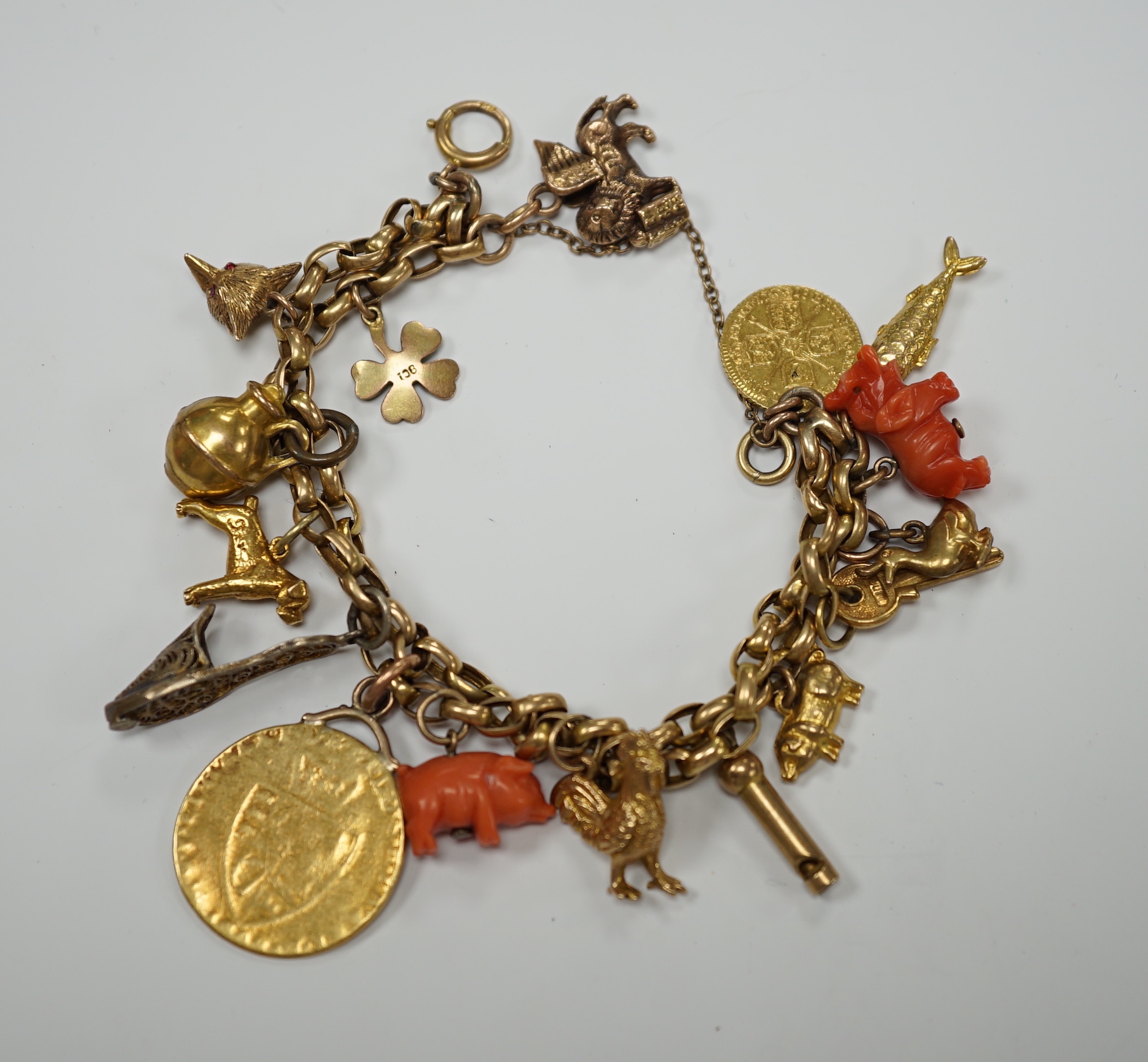 An early 20th century 9ct multi link charm bracelet, hung with sixteen assorted charms, including 9ct, coral, enamelled and a worn spade guinea